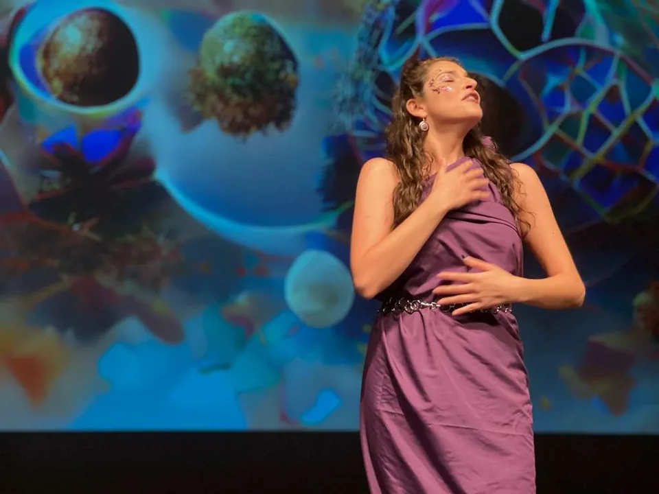 A festival soprano in a purple gown sings on stage in front of a colourful projected backdrop